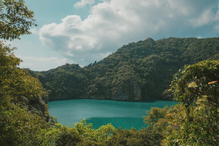 Serene lake surrounded by lush green hills under a partly cloudy sky.