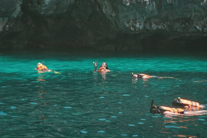 Snorkelers in clear turquoise water near rocky cliffs.