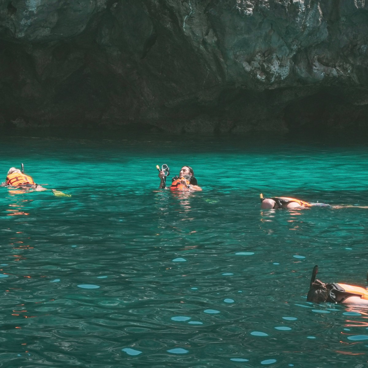 Snorkelers in clear turquoise water near rocky cliffs.