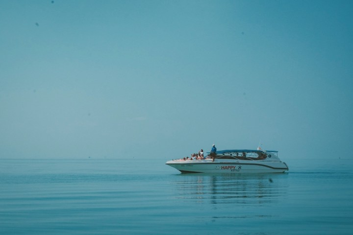 A small boat with passengers glides on calm, open water under a clear blue sky.