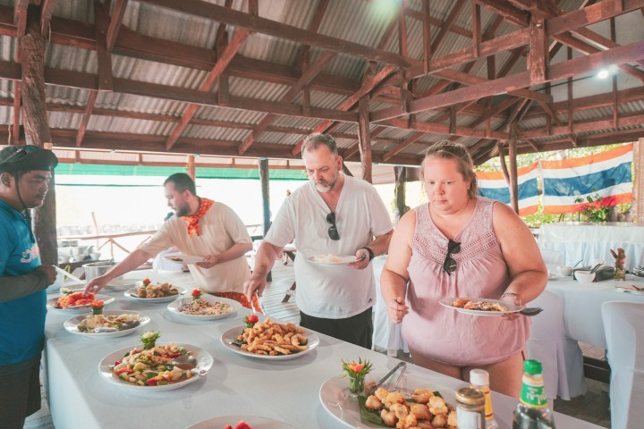 People serving themselves food from a buffet under a wooden pavilion.