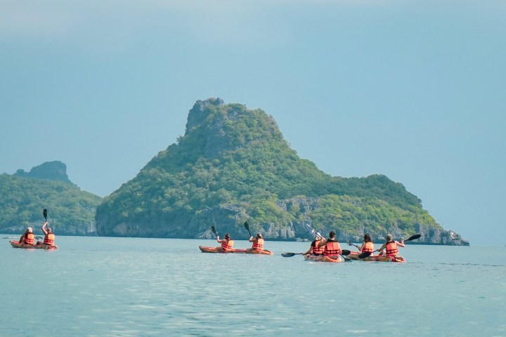 Kayakers in orange vests paddling near green islands on calm sea.