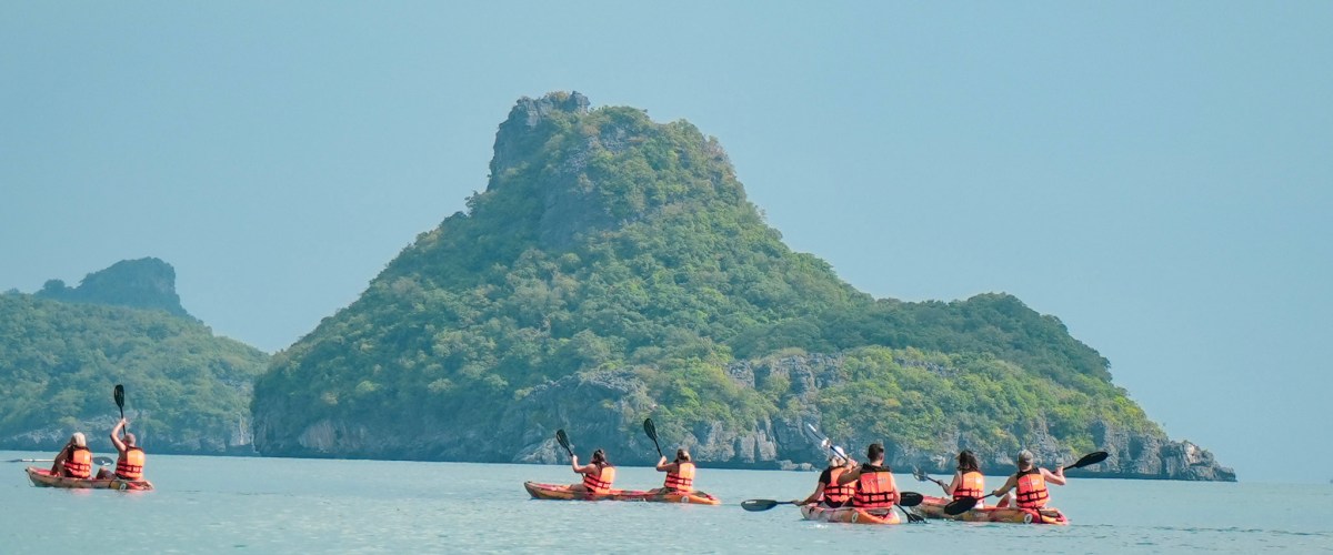 Kayakers in orange vests paddling near green islands on calm sea.