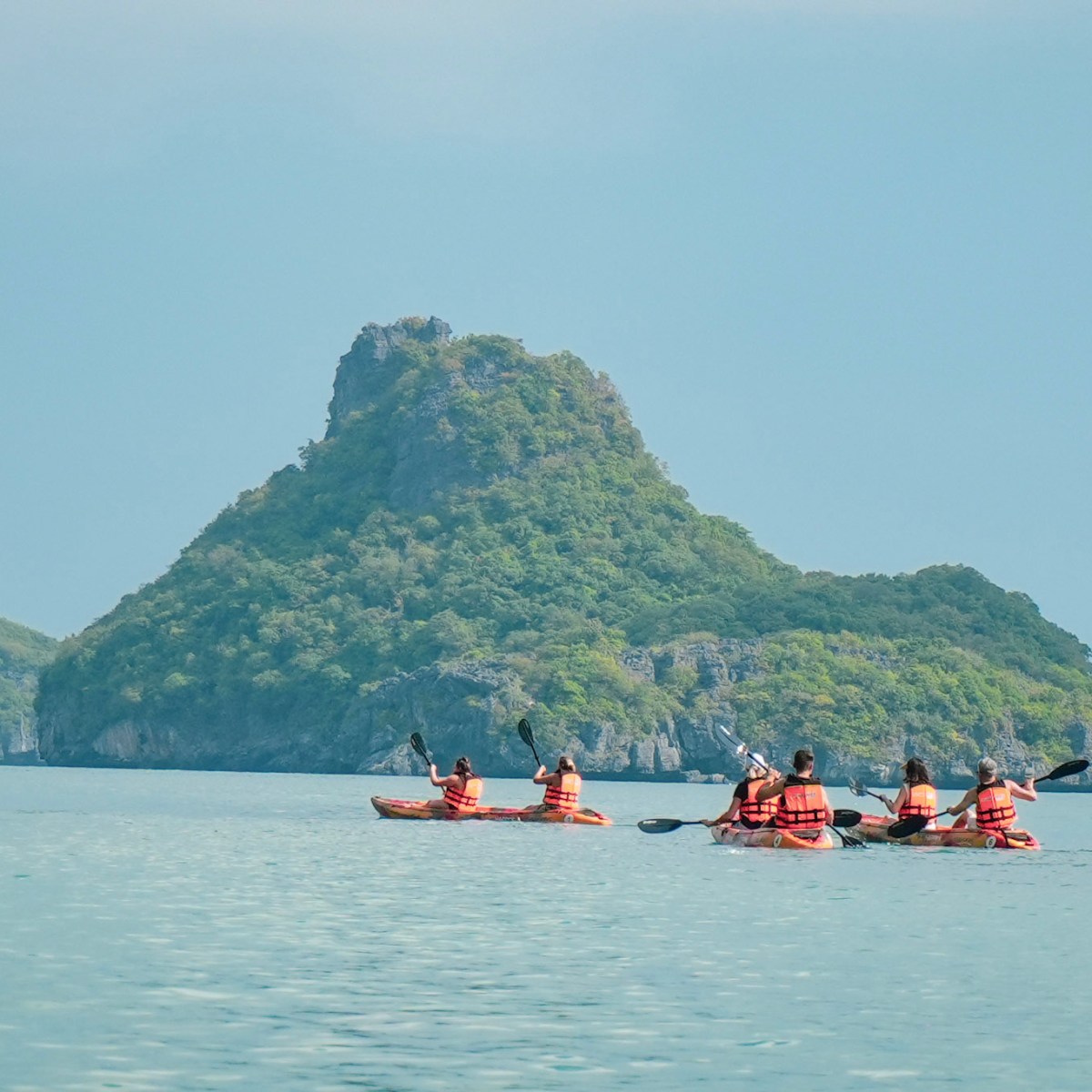 Kayakers in orange vests paddling near green islands on calm sea.