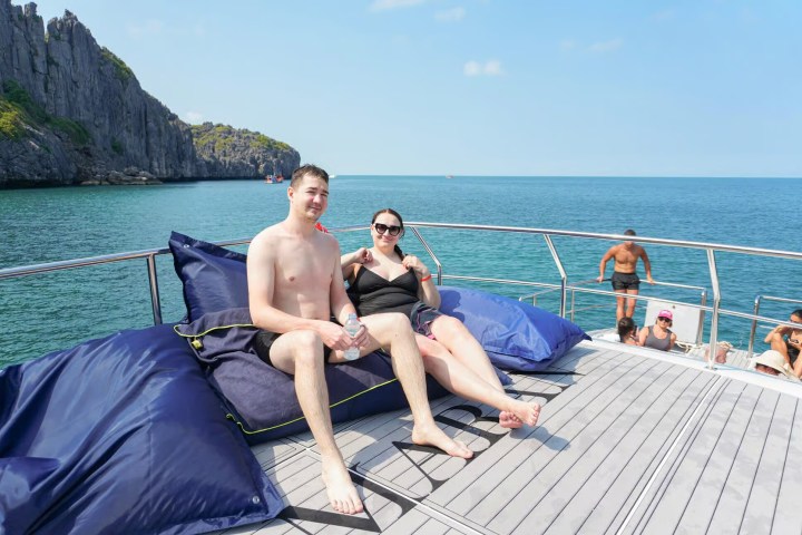 Two people relaxing on a boat deck with bean bags, scenic ocean view in the background.