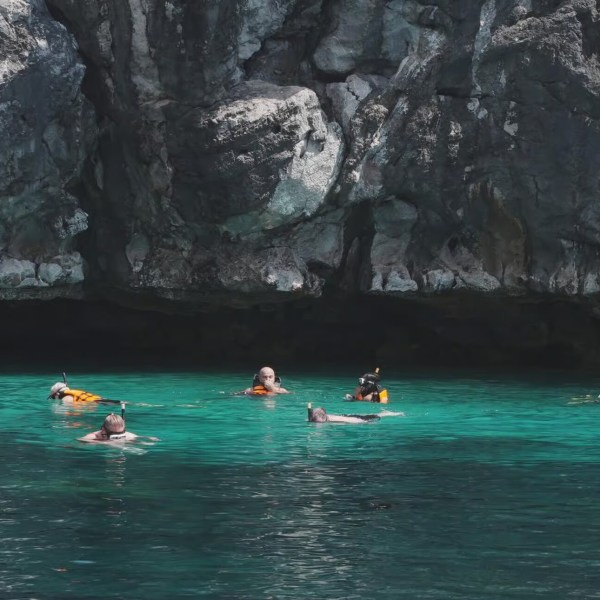 People snorkeling near rocky cliffs in clear turquoise water.