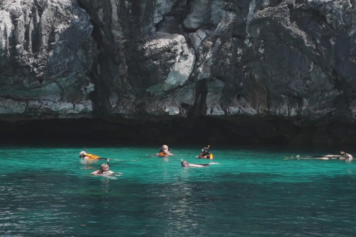People snorkeling near rocky cliffs in clear turquoise water.