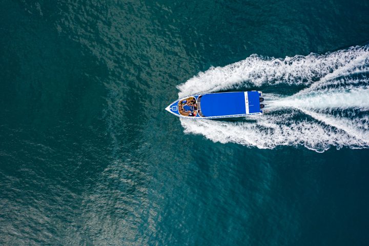 Aerial view of a blue speedboat moving through water, creating white waves.