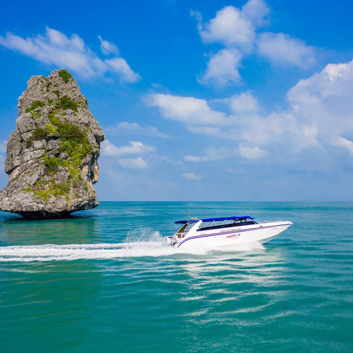 Speedboat cruising near a large rock in clear blue ocean under a bright sky.