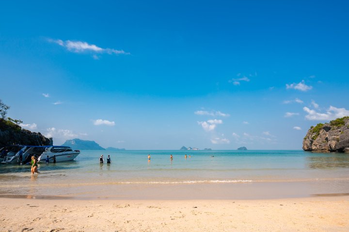 Sunny beach with people, speedboat, and distant islands on a clear day.