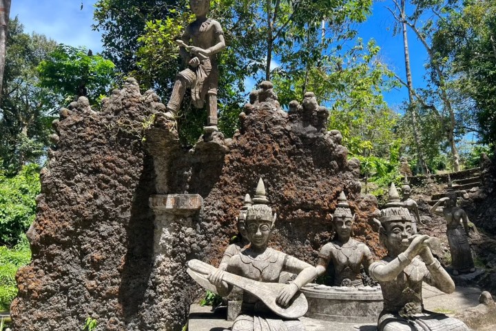 Stone statues of musicians and figures in a lush, outdoor setting.