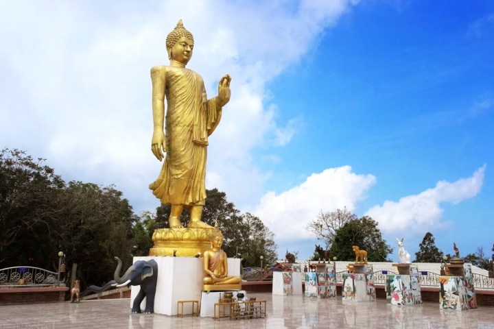 Large golden Buddha statue with smaller sculptures on a platform under a blue sky.