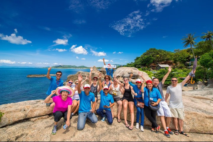 Group of people posing on rocks by the ocean under a clear blue sky.