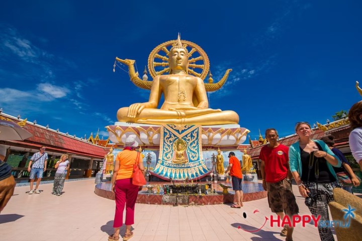 Large golden Buddha statue with people walking around, under a clear blue sky.