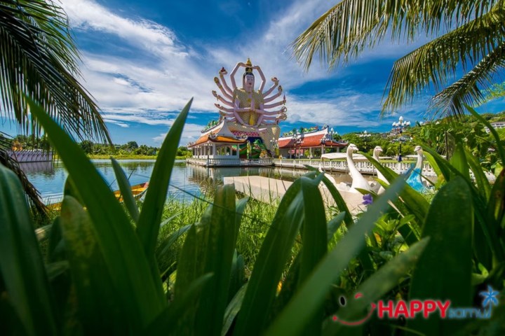 Tropical garden with a multi-armed statue near a lake under a blue sky.