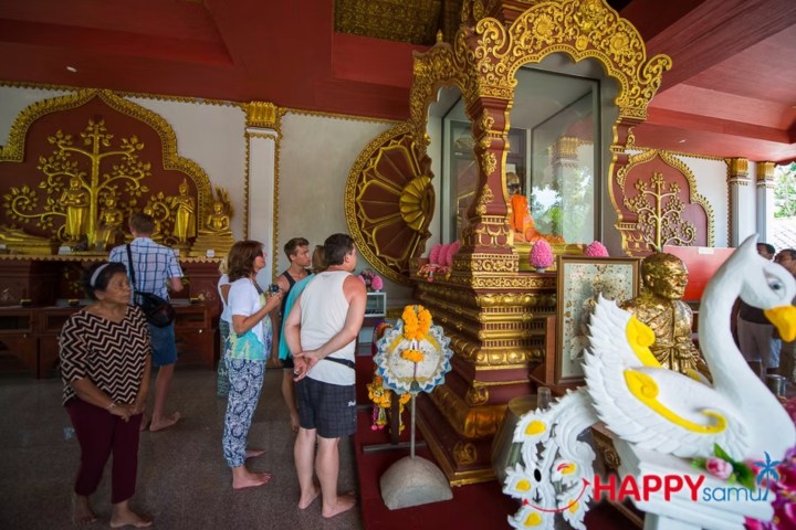 Tourists admire ornate golden shrine with decorations inside a temple.