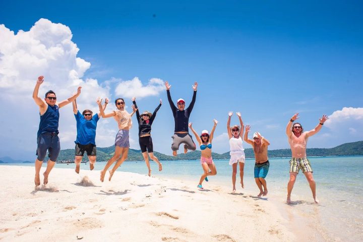 Group of people joyfully jumping on a sandy beach under a clear blue sky.