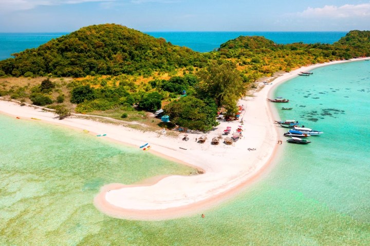 Aerial view of a sandy beach with turquoise water and lush green hills.
