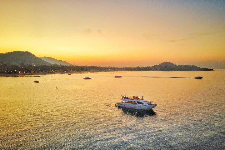 Boat on calm water at sunset with mountains in the background.