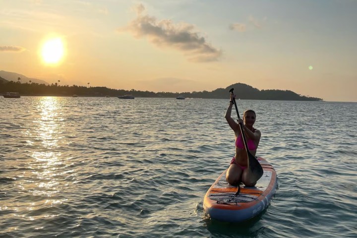 Person paddleboarding on calm sea at sunset, with an island in the background.