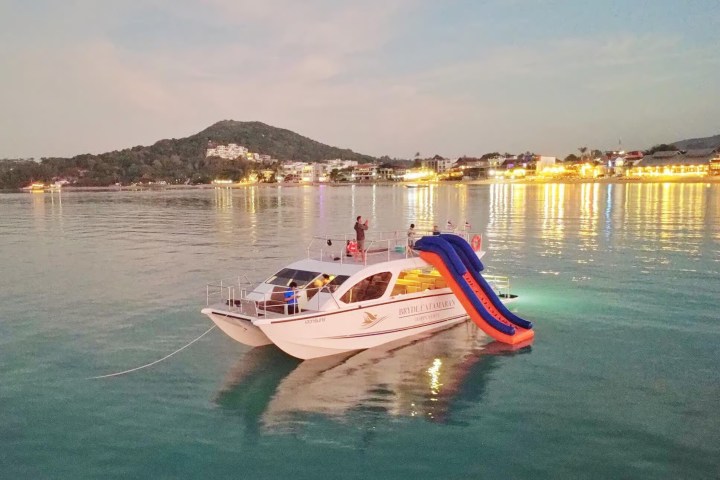 Boat with water slide floats near a coastal town at dusk.