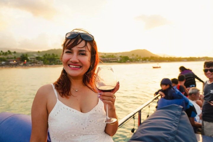 Woman in white dress holding wine glass on a boat during sunset.