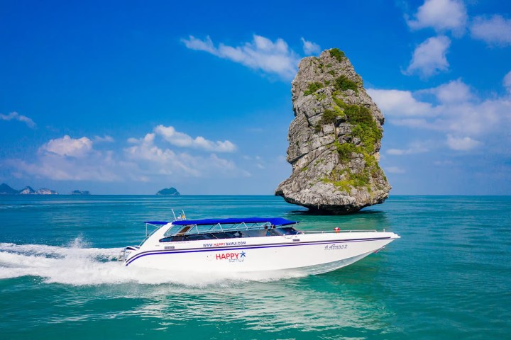 Speedboat on turquoise sea near a tall rock formation under blue sky.
