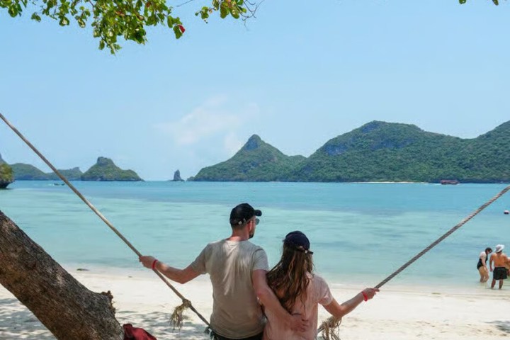 Couple on a beach swing with ocean and mountains in the background.