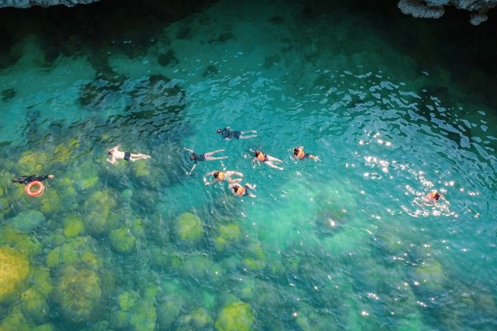 Aerial view of people snorkeling in clear, green water over rocks.