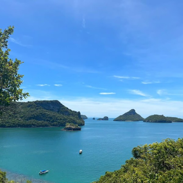 Tropical seascape with islands, blue sky, and boats on calm water.