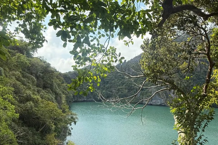 Scenic view of a turquoise lake surrounded by lush green trees and hills under a partly cloudy sky.