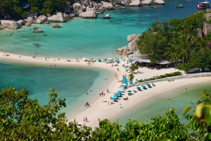 Aerial view of a tropical beach with turquoise water and sunbathers on white sand.