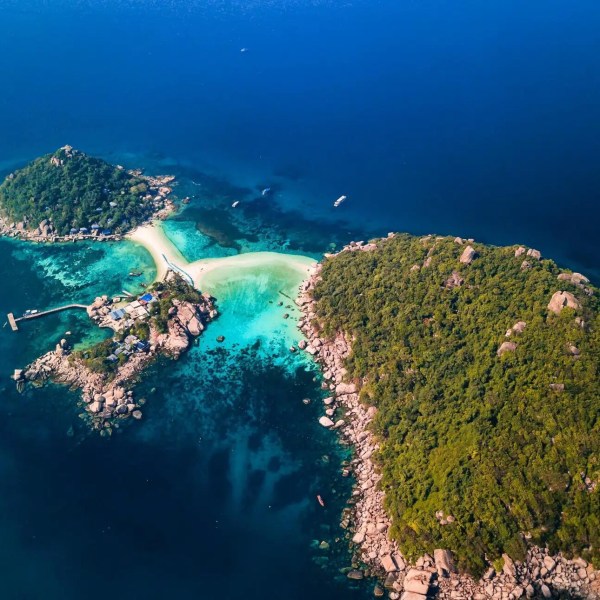 Aerial view of two lush islands connected by a sandy beach in blue ocean.