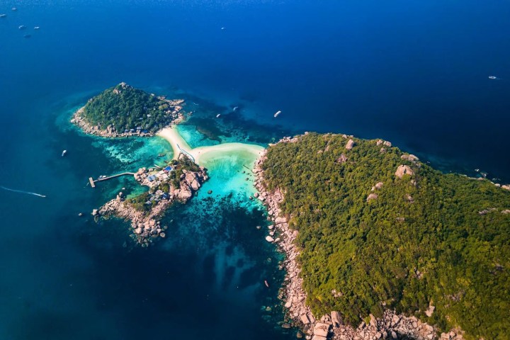 Aerial view of two lush islands connected by a sandy beach in blue ocean.