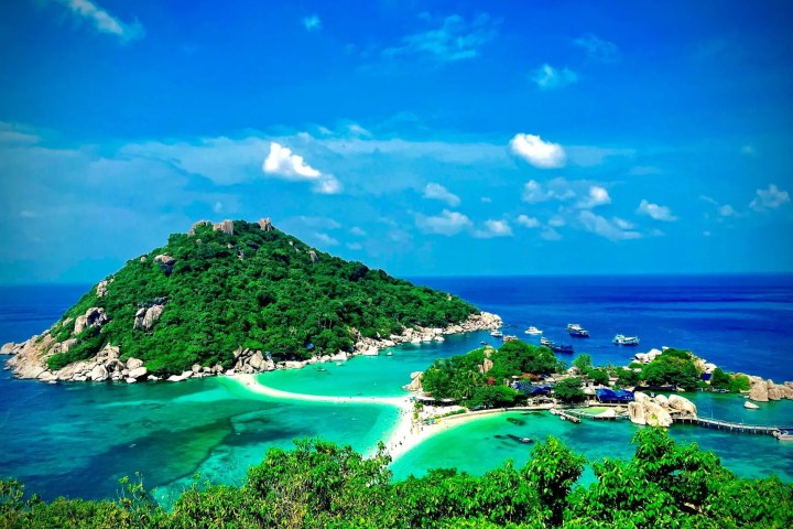 Tropical island with lush greenery surrounded by turquoise ocean under a clear blue sky.