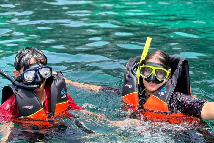 Two people snorkeling in clear water with life vests and masks.