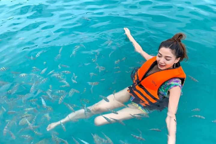 Person in an orange life jacket swimming with fish in clear blue water.