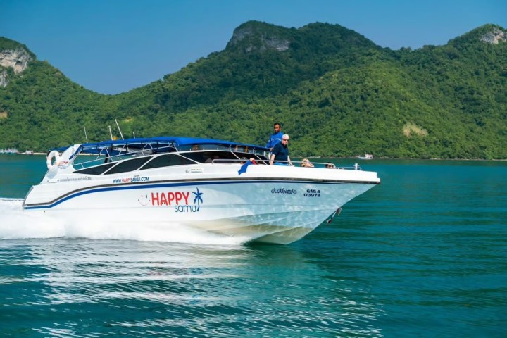 Speedboat named 'Happy Samui' cruising on blue water, green hills in background.