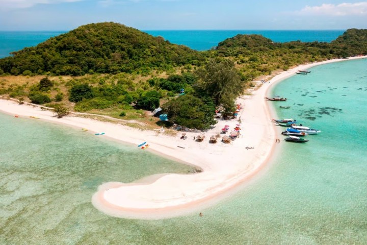 Aerial view of a beach with boats, umbrellas, and green hills in the background.