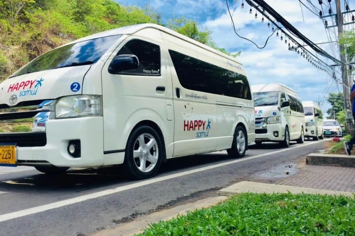 Three white minibuses labeled 'HAPPY Samui' parked on a road.