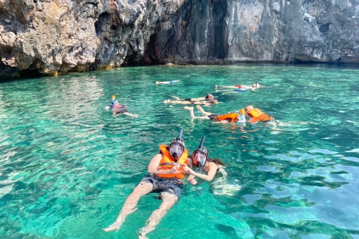 People snorkeling in clear turquoise water near rocky cliffs.