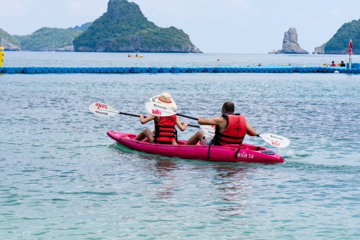 Two people kayaking on calm water with island in background.
