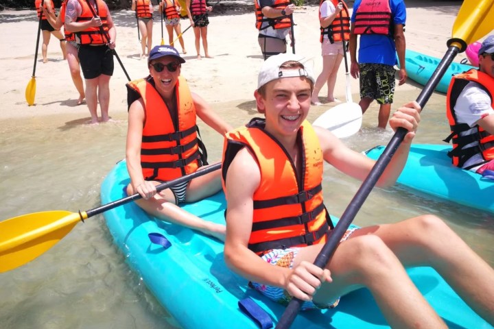 Group of people kayaking on a beach, wearing orange life vests.