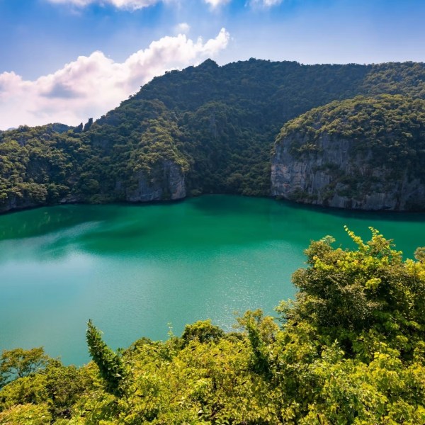 Scenic view of a turquoise lake surrounded by lush green hills under a blue sky.