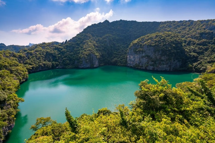 Scenic view of a turquoise lake surrounded by lush green hills under a blue sky.