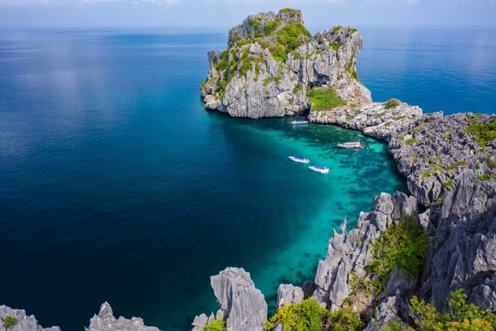 Aerial view of rocky island with turquoise water and boats.