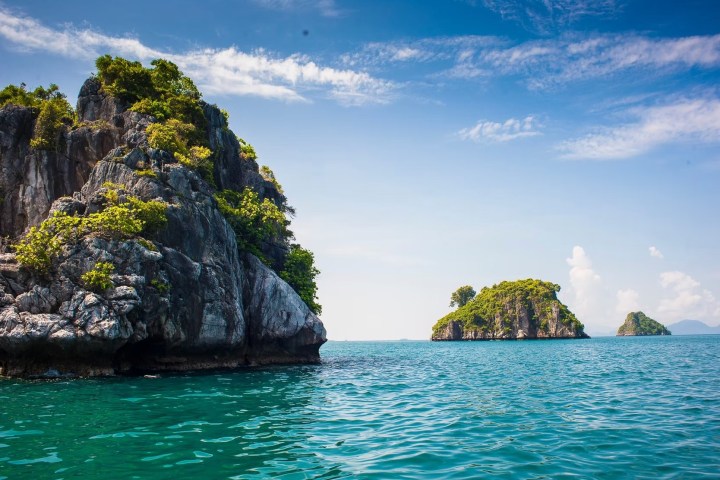 Ocean view with rocky islands covered in greenery under a blue sky.