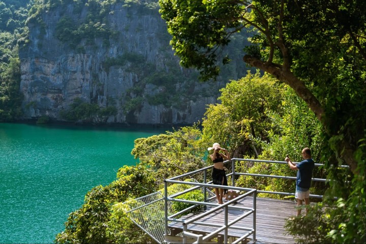 People on a viewing platform overlooking a turquoise lake and lush cliffs.