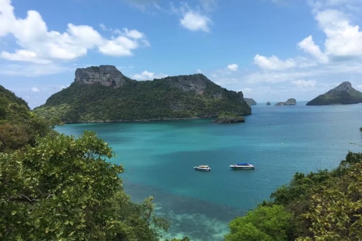 Tropical bay with boats, green islands, and blue sky with clouds.