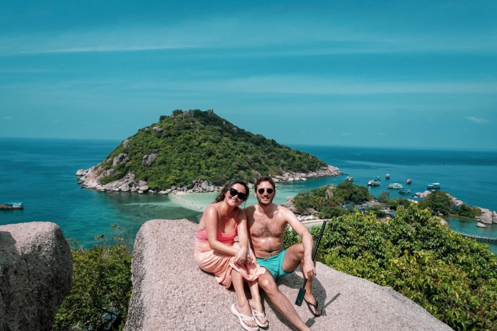 Couple sitting on rock with ocean and small island in background.